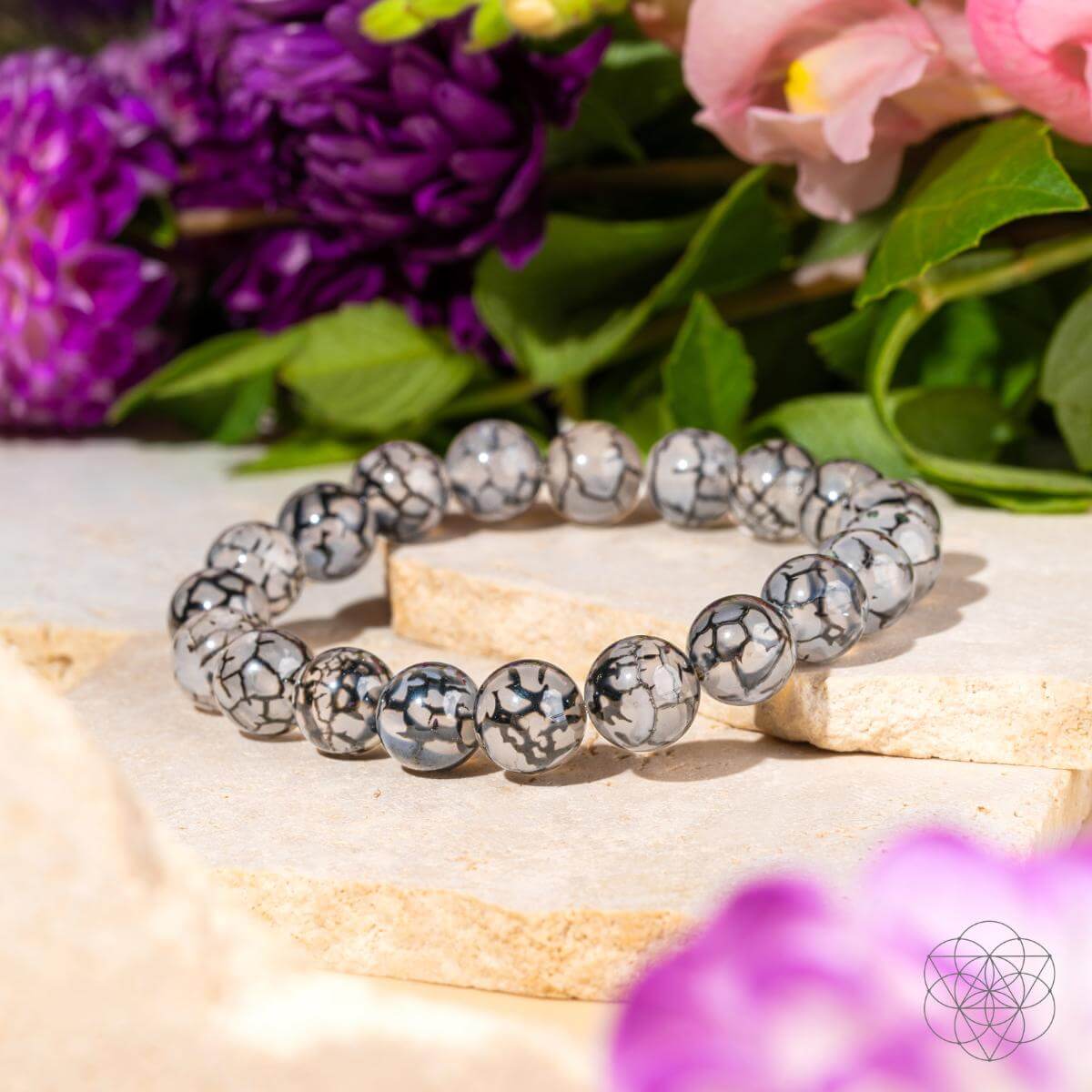Bracelet with gray beads on a wooden surface with flowers in the background