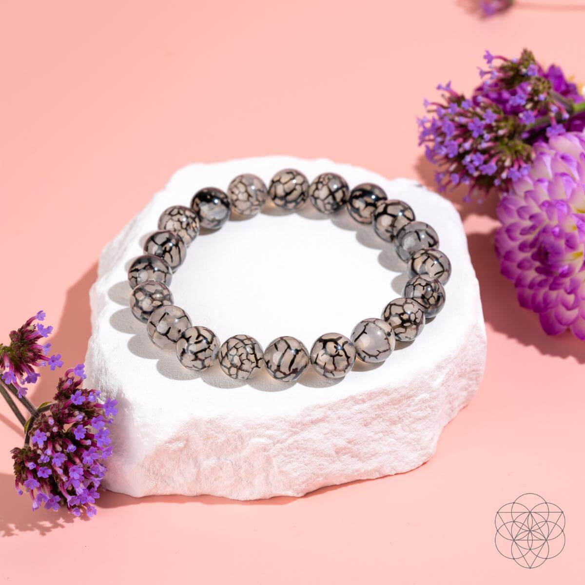 Bracelet with textured beads on a white stone surrounded by purple flowers on a pink background