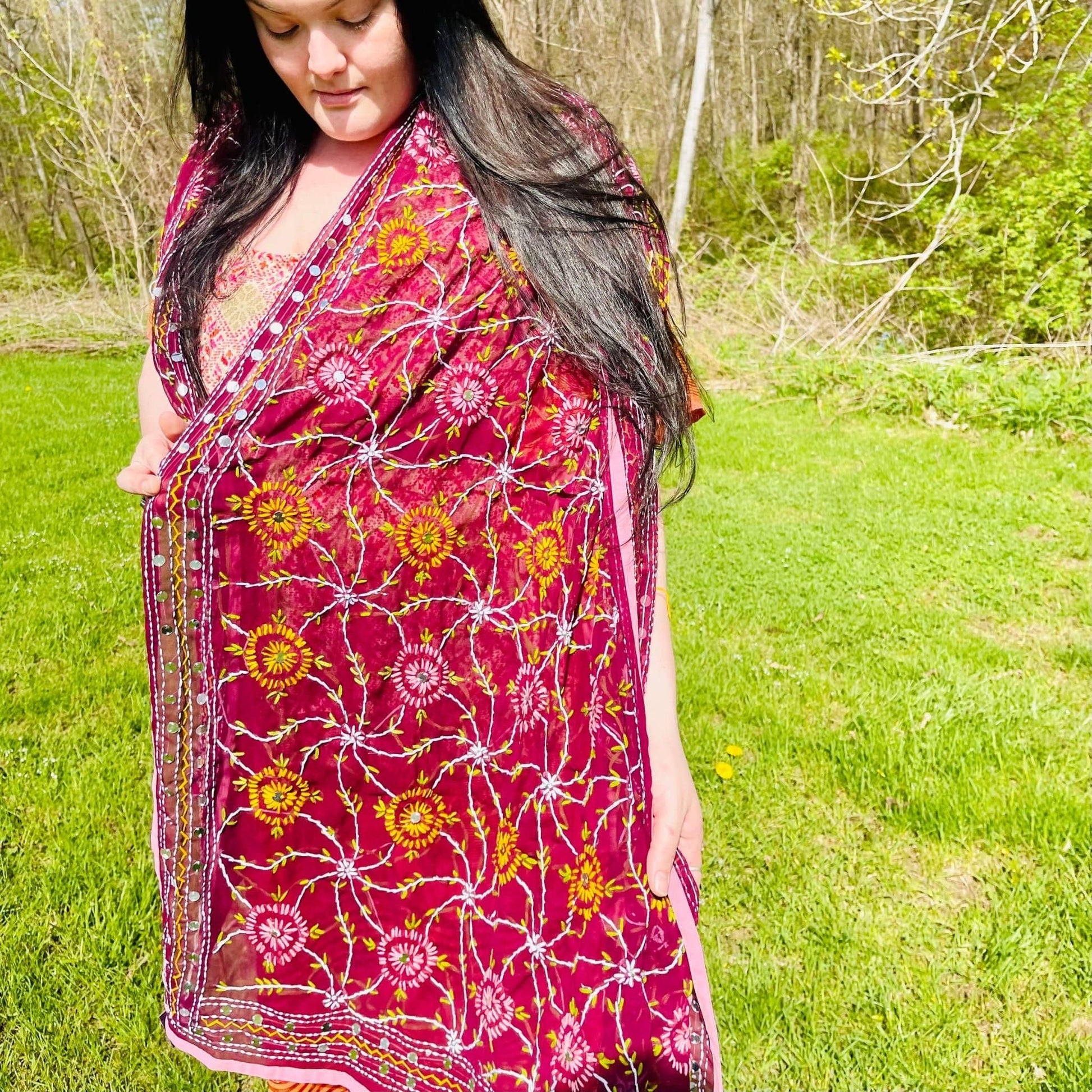 Woman wearing a pink floral dress standing in a grassy outdoor area.