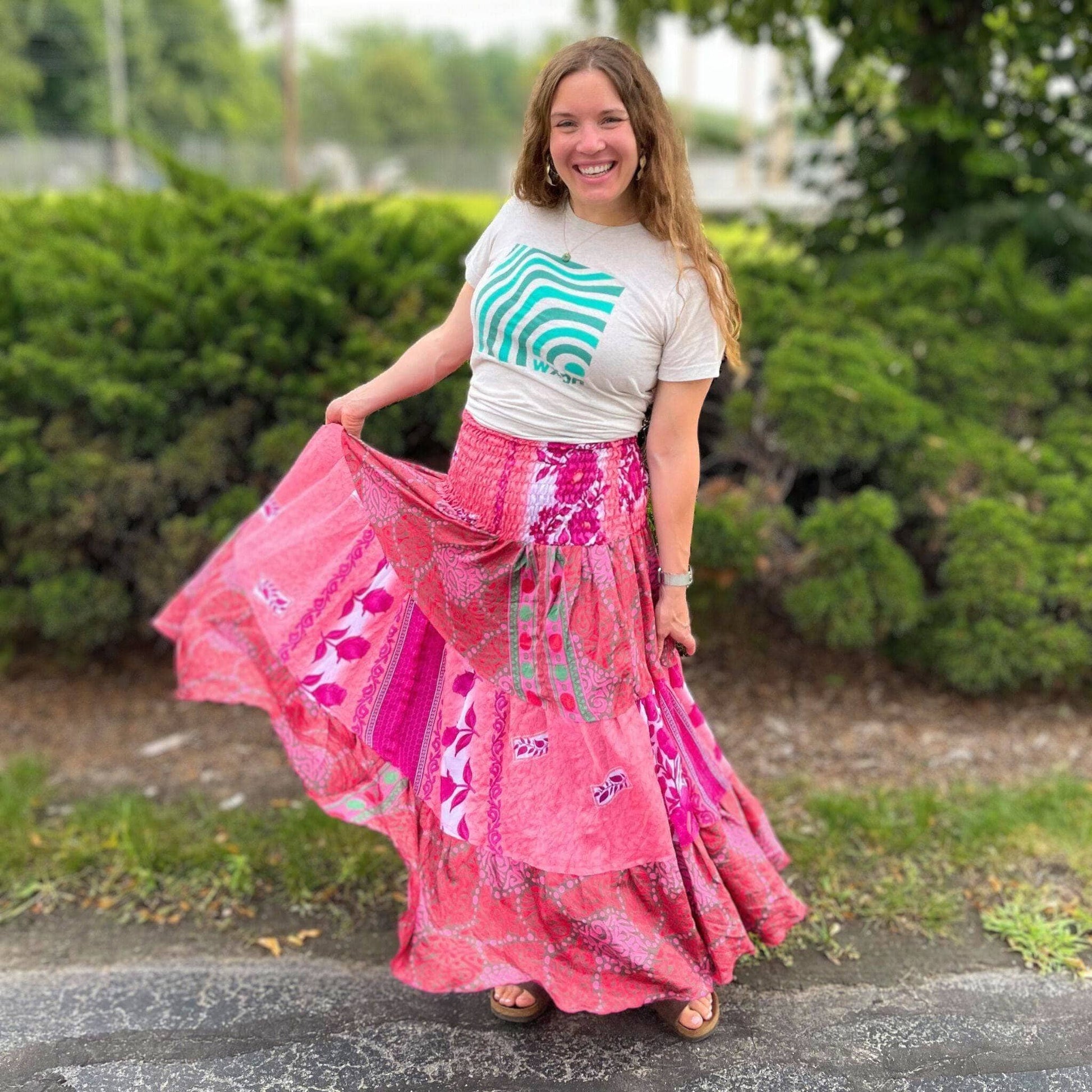 Woman wearing a pink floral skirt and white t-shirt with green design outdoors.