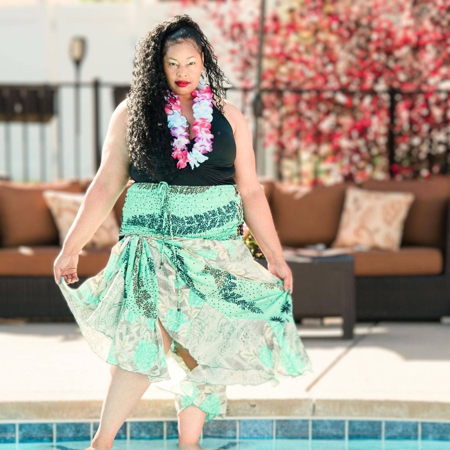 Woman in a green floral dress standing by a pool with a colorful background