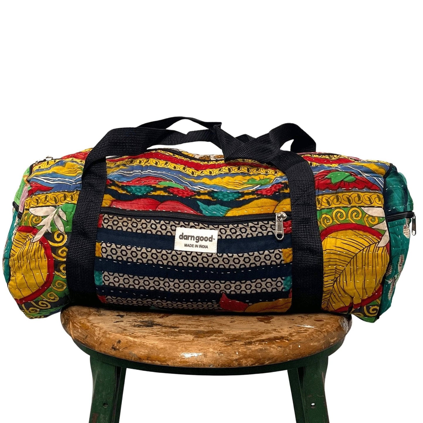 Colorful duffel bag with patterned design on a wooden stool against a white background