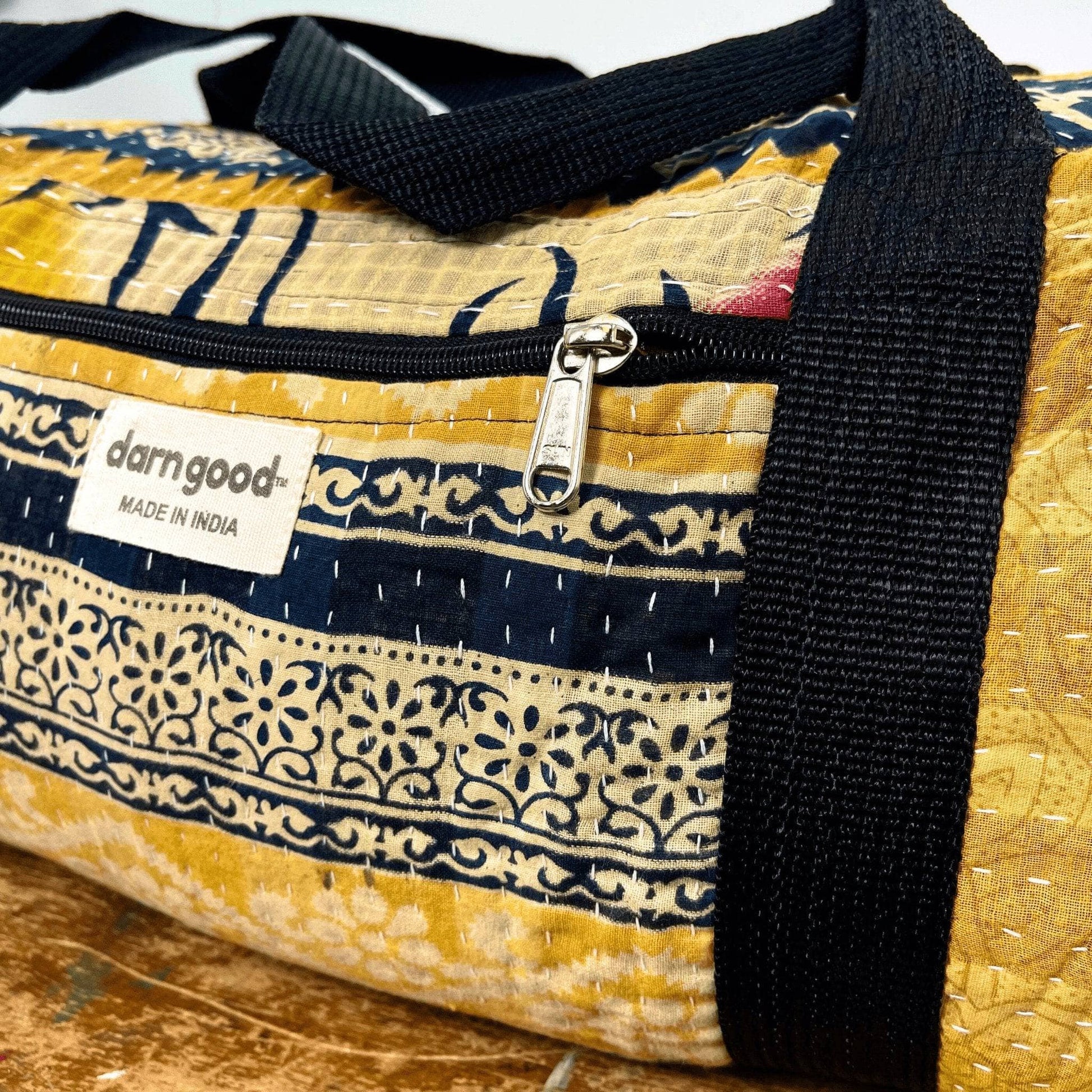 Patterned bag with black strap and 'darngood' label on a wooden surface