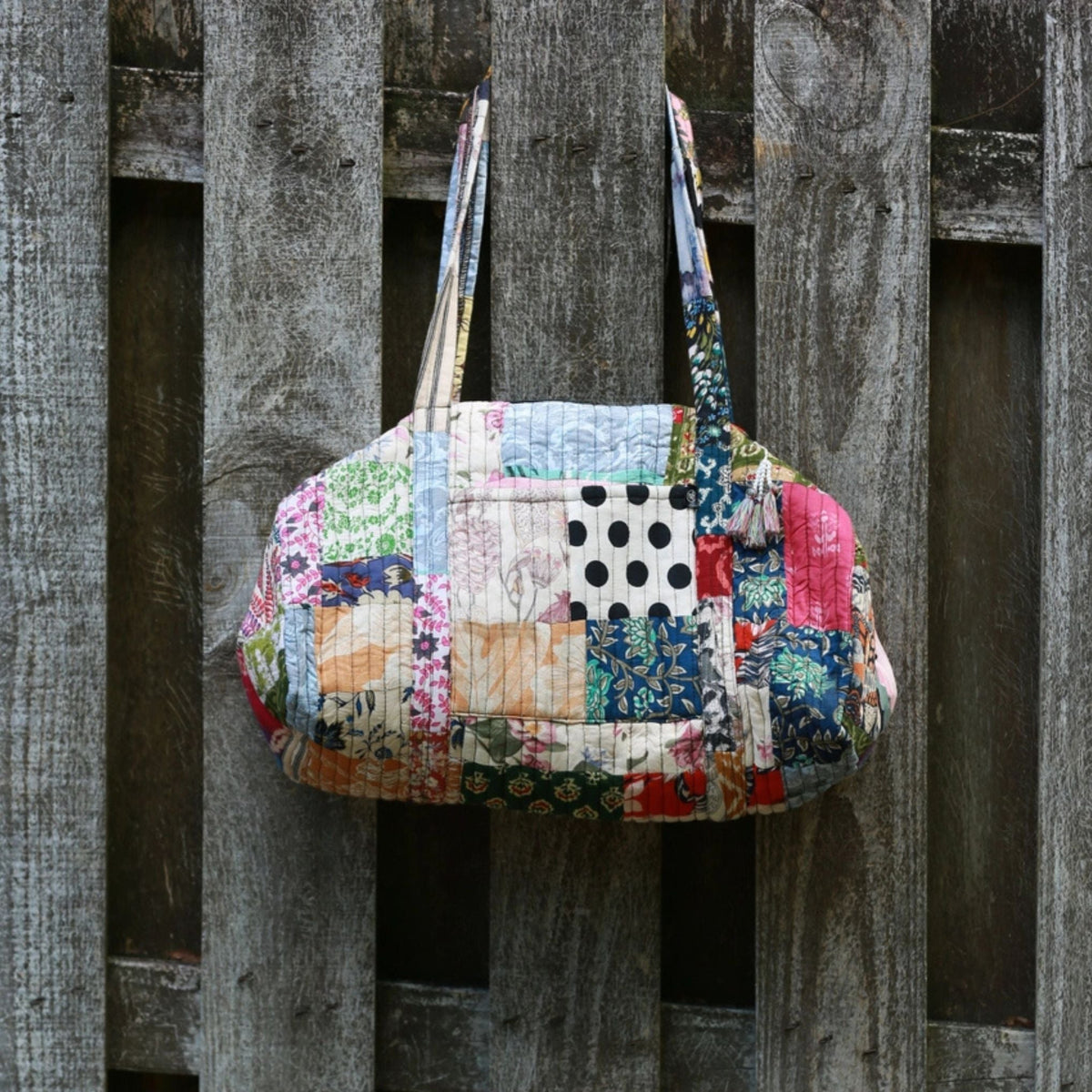 Patchwork handbag with floral and polka dot patterns hanging on a wooden fence.