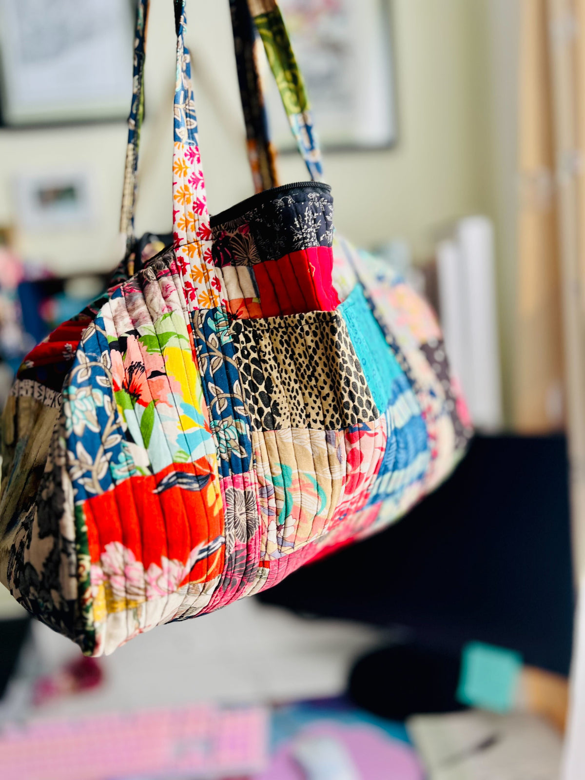 Colorful patchwork handbag with floral and animal print patterns on a blurred indoor background.