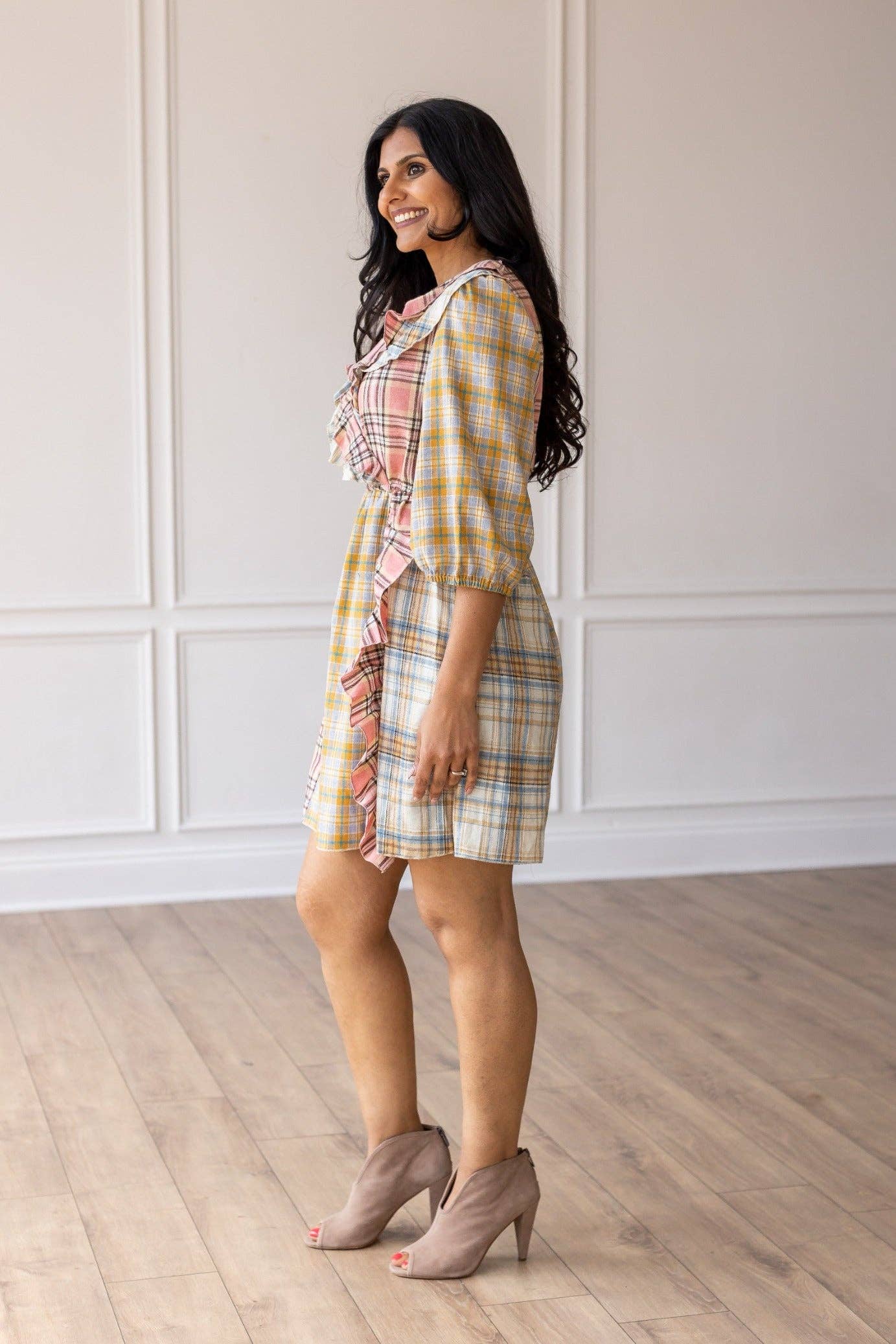 Woman wearing a plaid dress standing in a room with wooden flooring and white paneled walls.