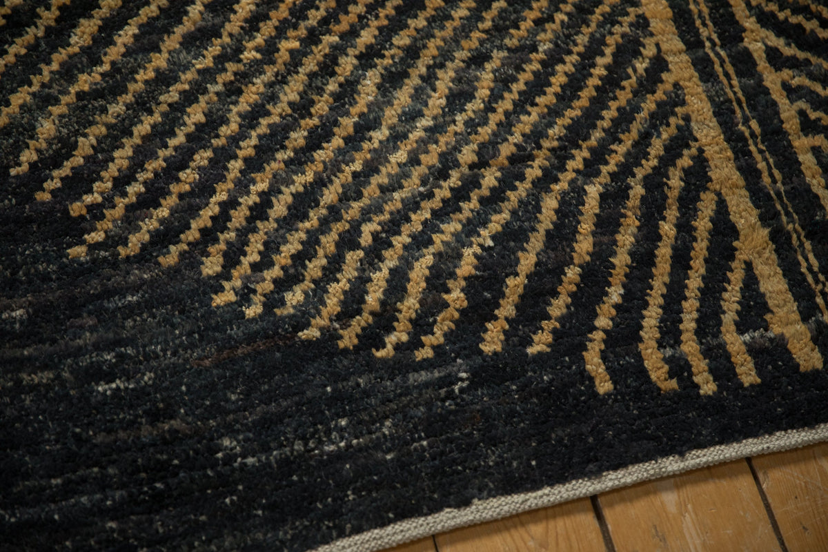 Close-up of a black and gold patterned rug on a wooden floor.