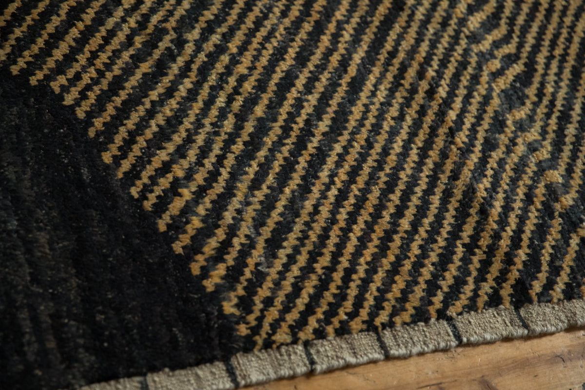 Close-up of a textured black and brown rug on a wooden floor.