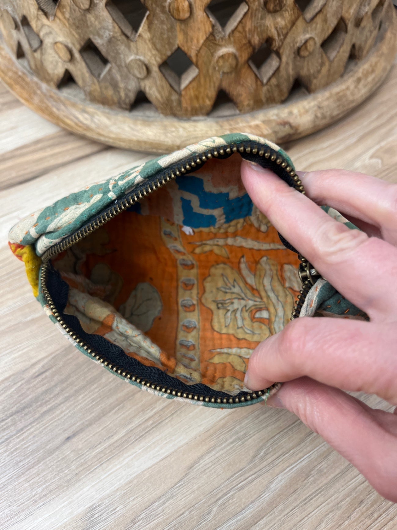 Hand holding a small fabric pouch with intricate patterns on a wooden surface