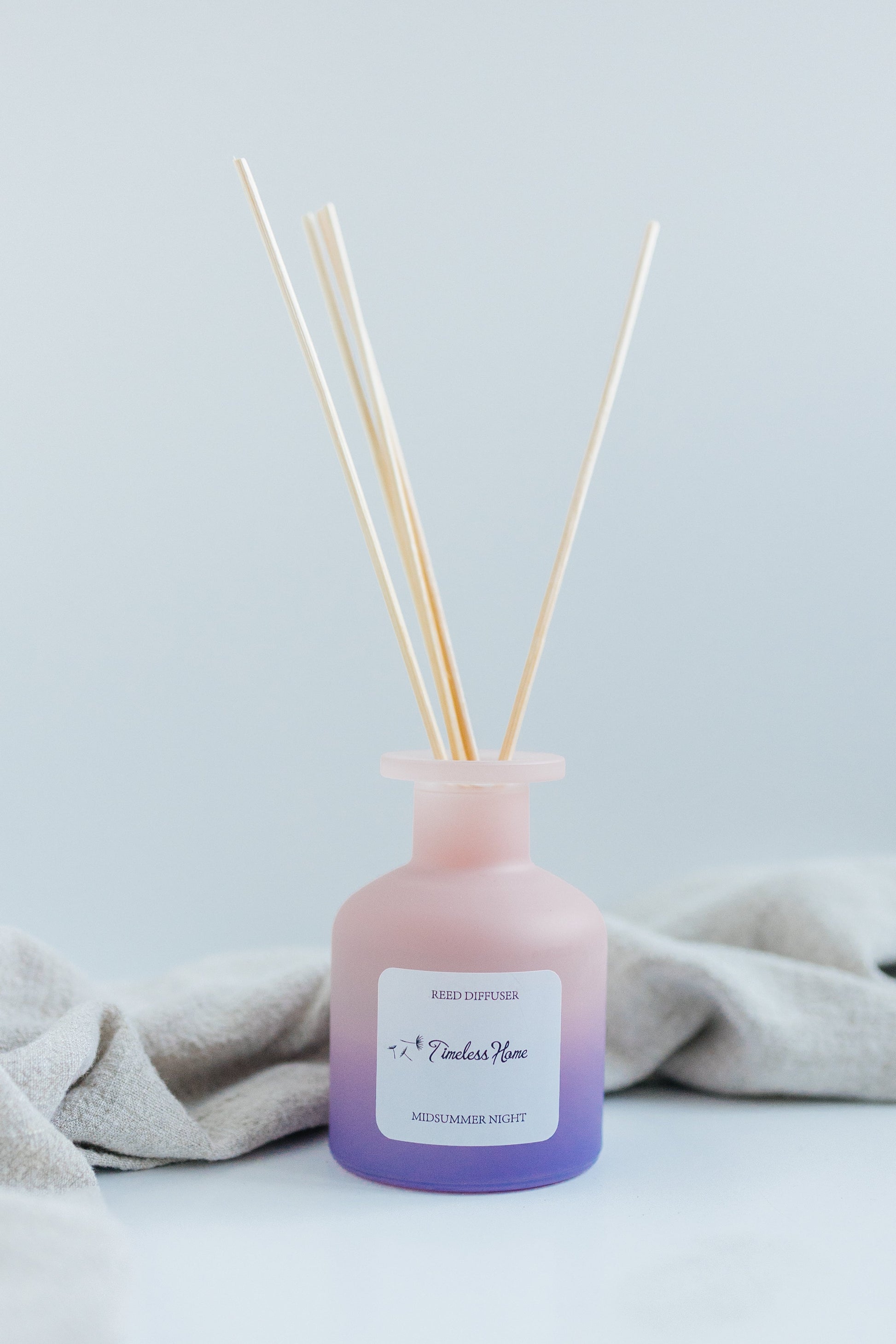 Pink and purple diffuser bottle with wooden sticks on a light gray background