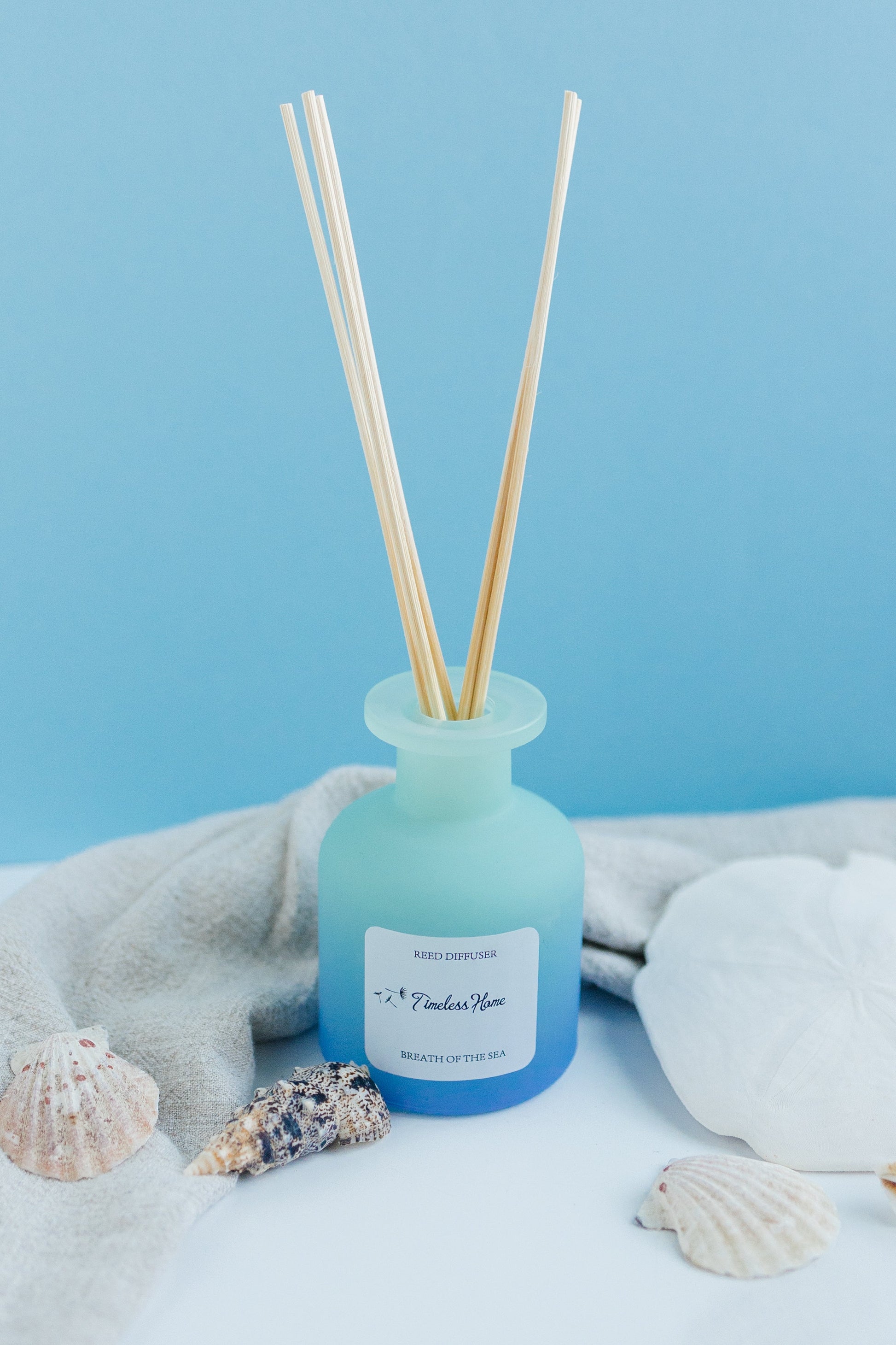 Reed diffuser with wooden sticks in a light blue bottle on a light blue background with seashells.