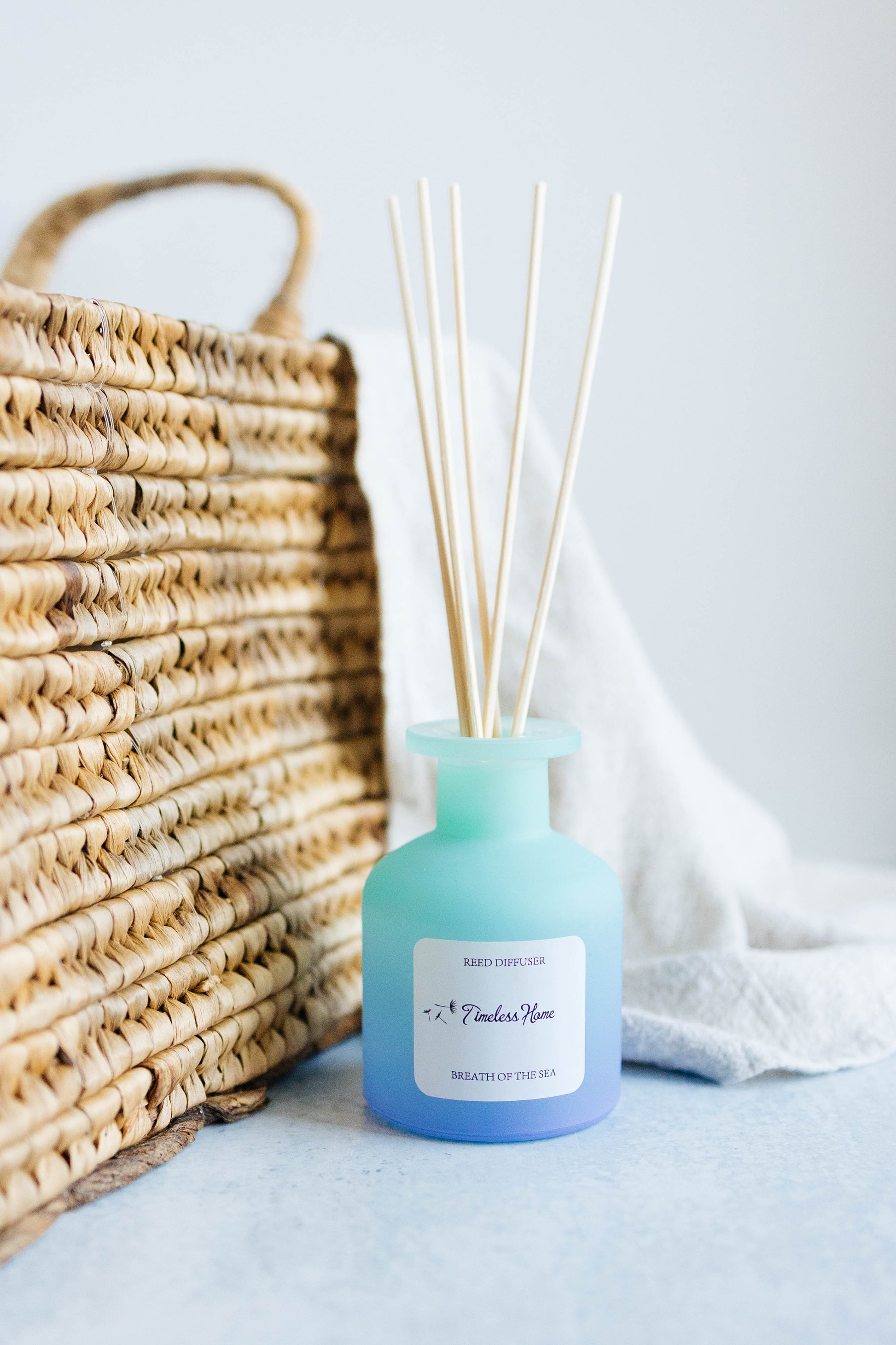 Blue diffuser bottle with reeds on a light surface next to a woven basket.