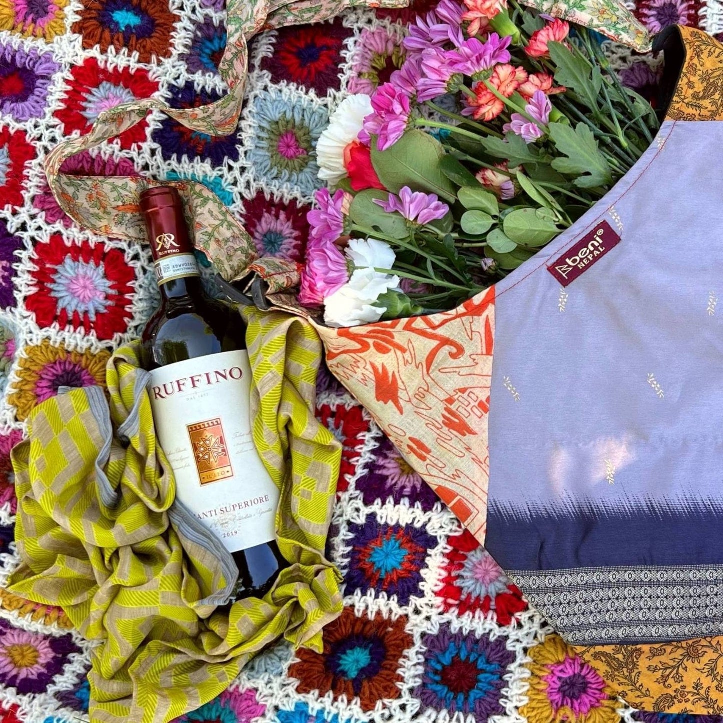 Bottle of Ruffino wine, colorful blanket, and flowers on a textured surface