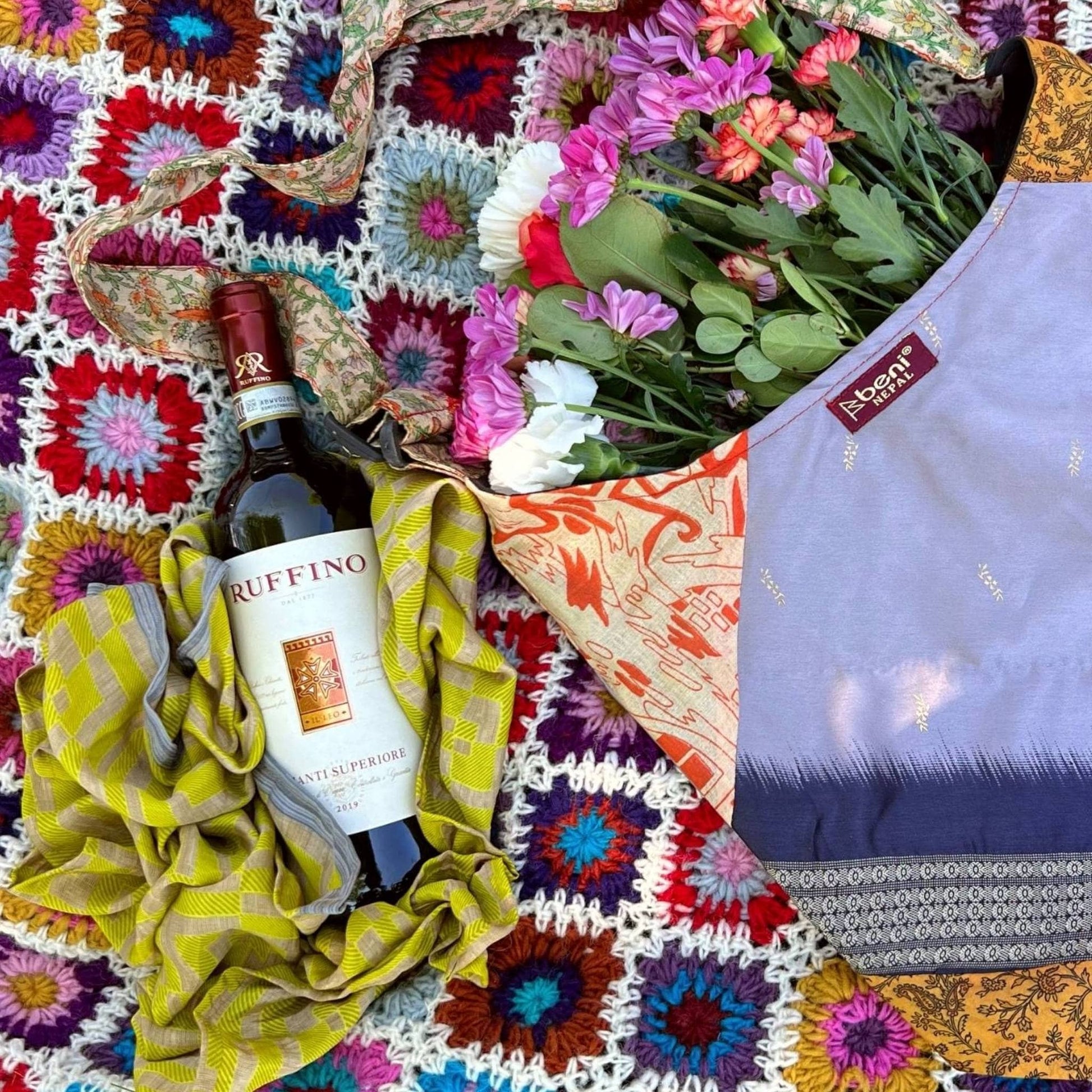 Bottle of Ruffino wine, colorful blanket, and flowers on a textured surface