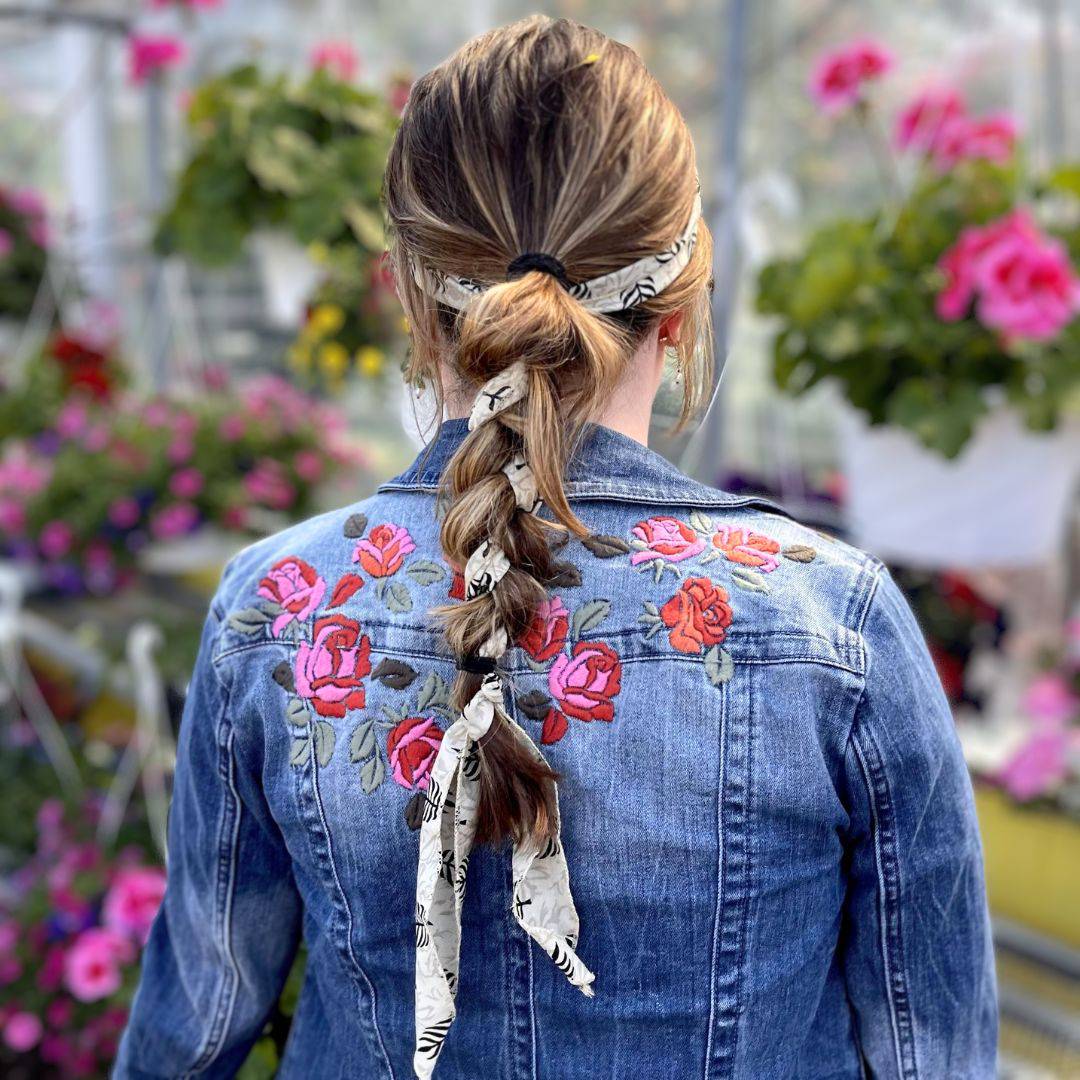 Person wearing a blue denim jacket with floral embroidery in a greenhouse setting