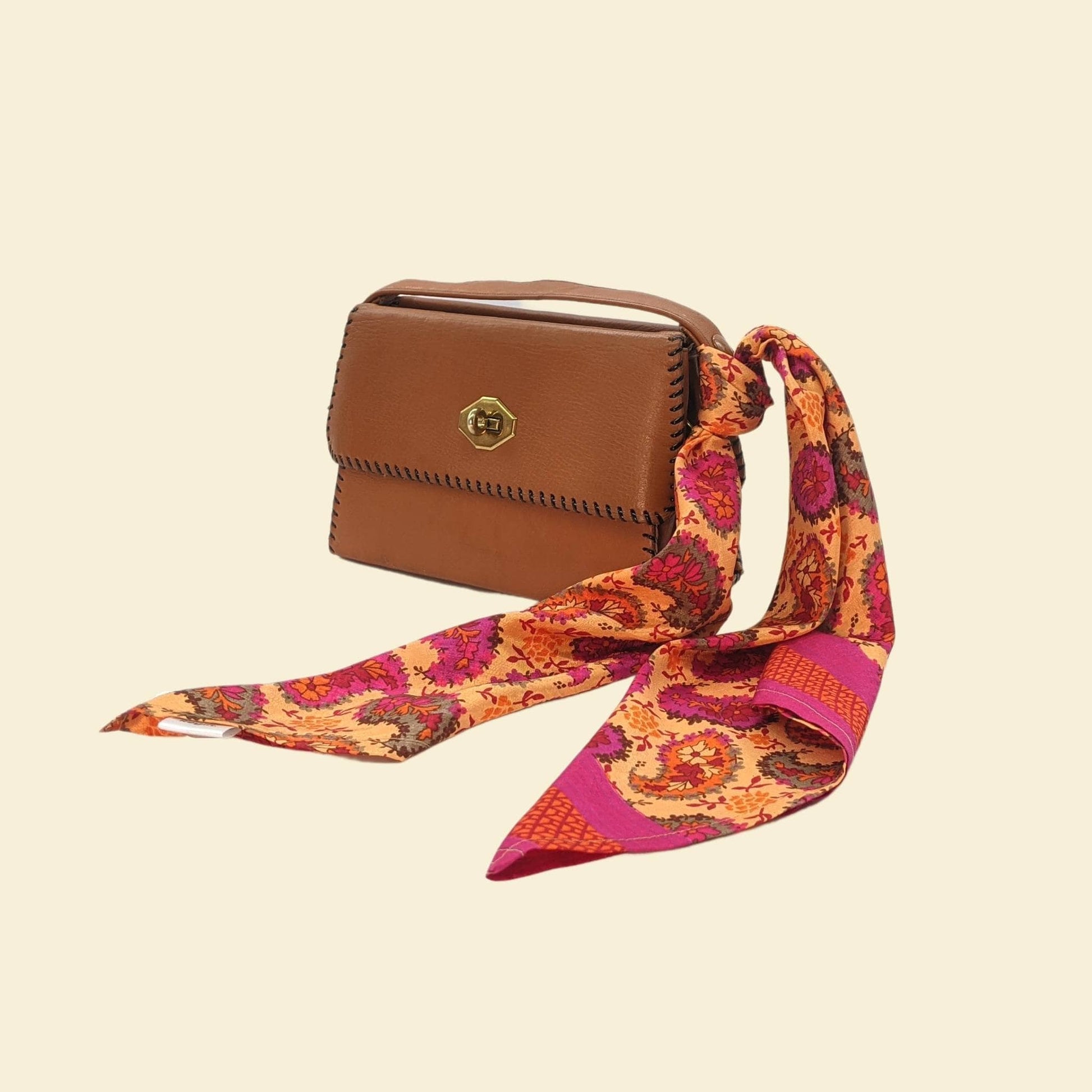 Brown handbag with a colorful scarf draped over it on a beige background