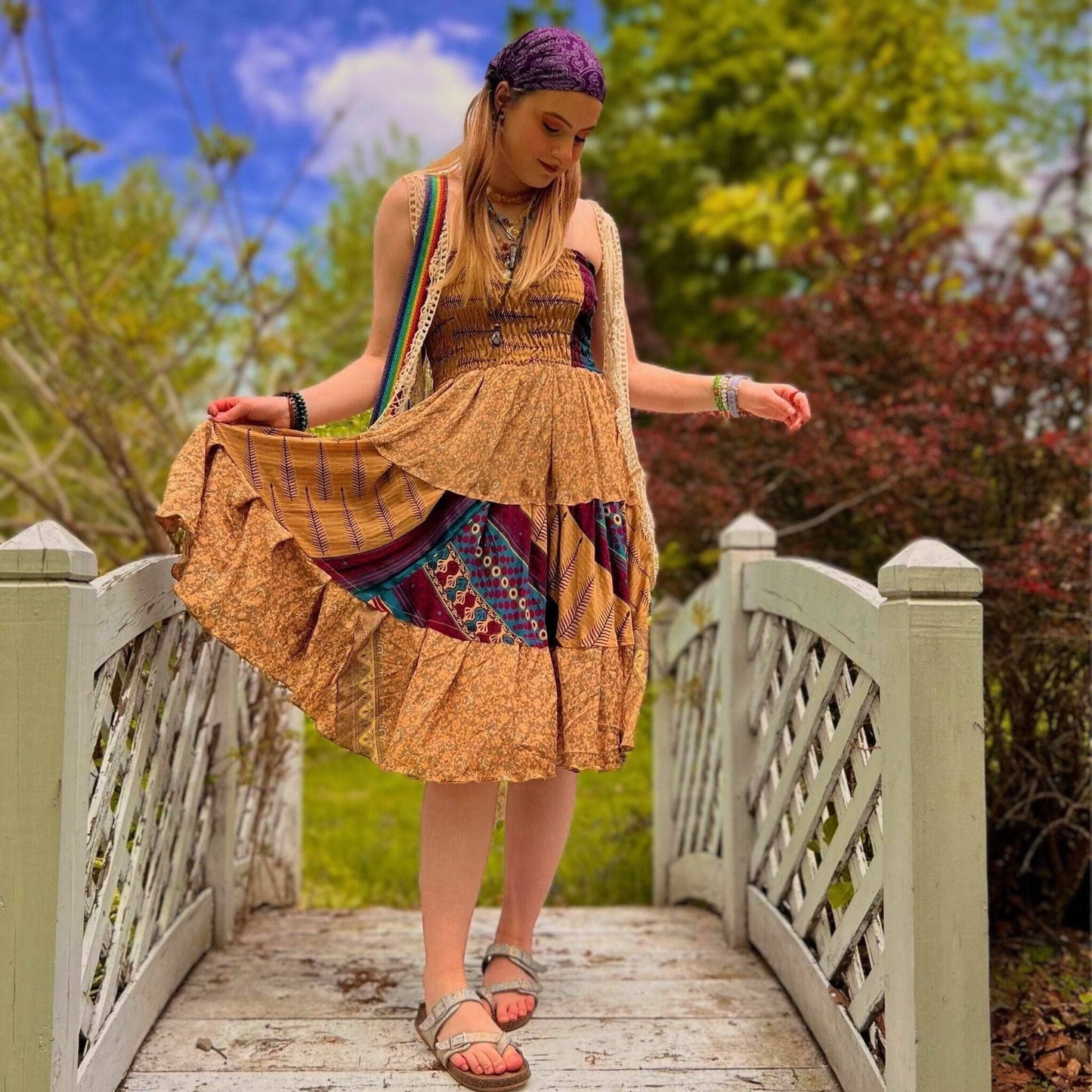 Woman in a patterned dress standing on a wooden bridge with trees and blue sky in the background