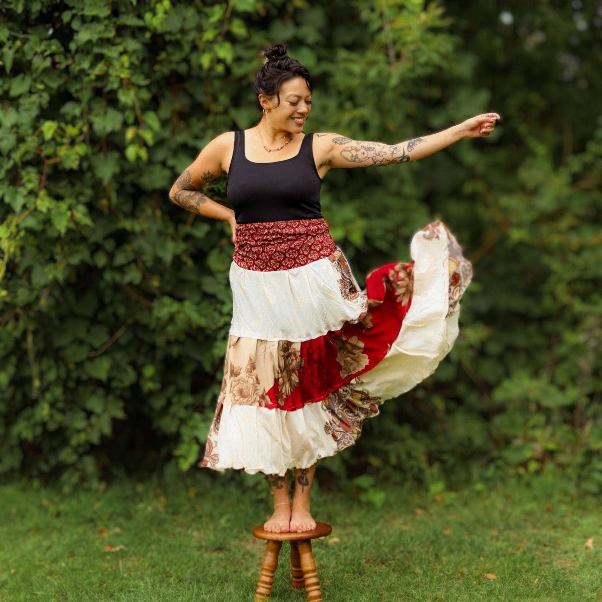 Woman in a colorful skirt standing on a stool outdoors with greenery in the background