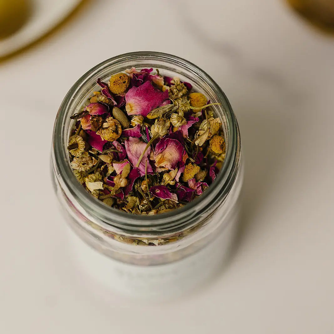 Glass jar filled with dried flowers and herbs on a light surface