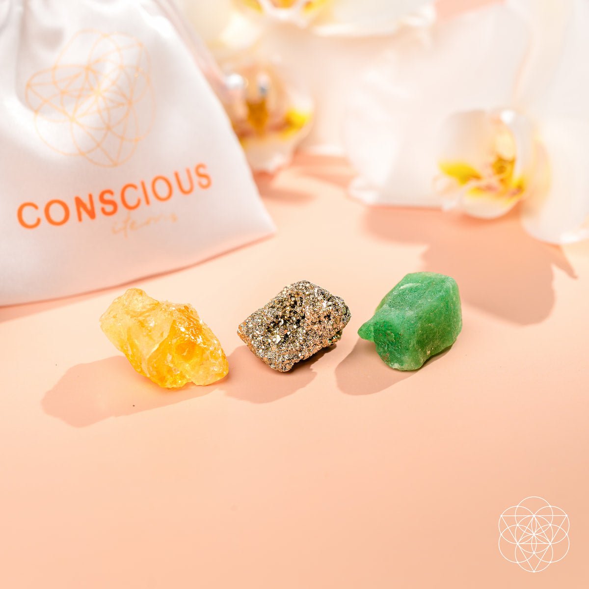 Three colorful crystals on a pink surface with 'Conscious' branding in the background.