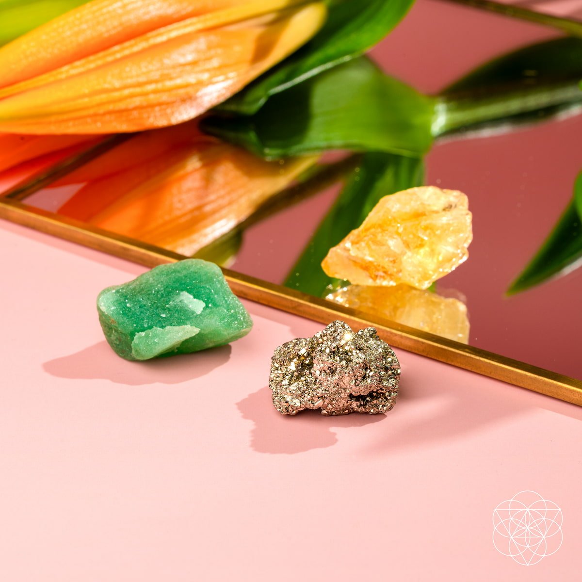 Three different colored crystals on a pink surface with a flower in the background