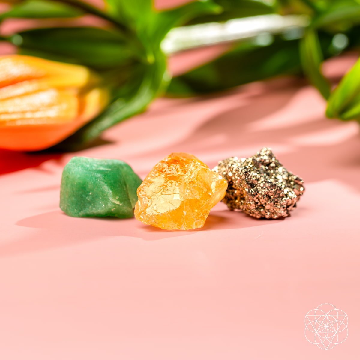 Three colorful crystals on a pink surface with blurred flowers in the background