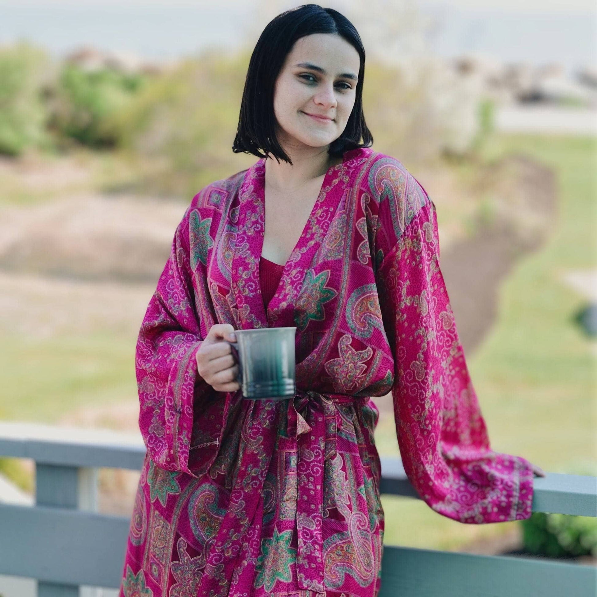 Woman in a pink patterned robe holding a mug outdoors