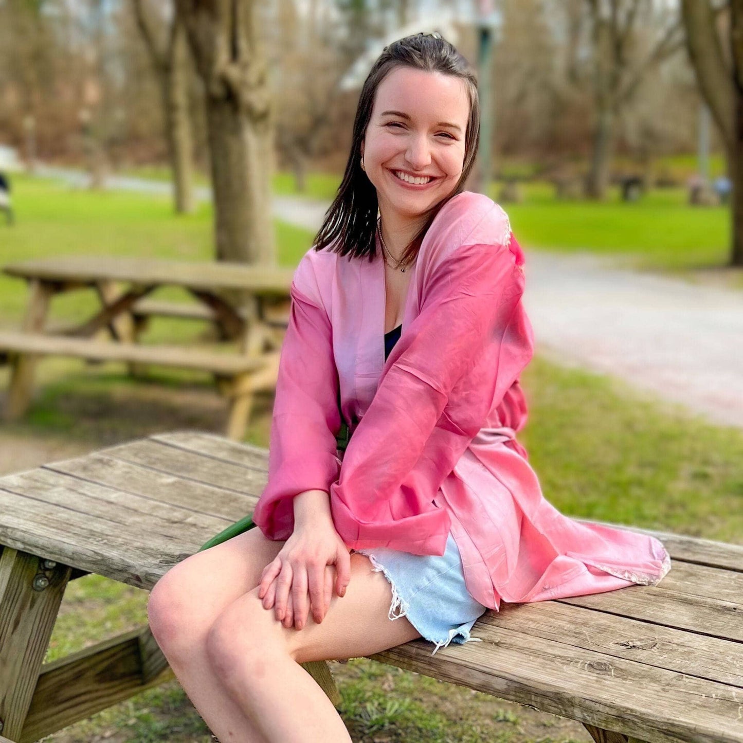 Woman in a pink jacket sitting on a wooden bench in a park