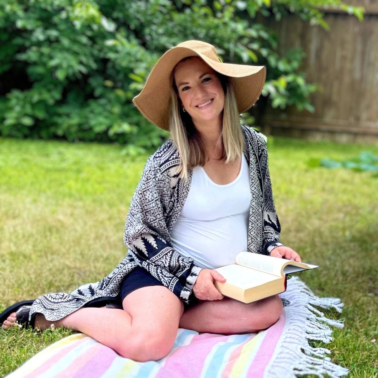 Woman sitting on a blanket in a garden, reading a book