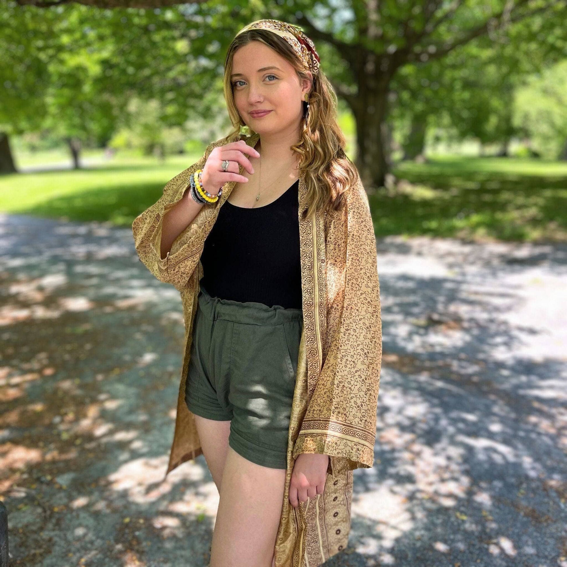 Woman standing outdoors in a park wearing a patterned shawl, black top, and green shorts.