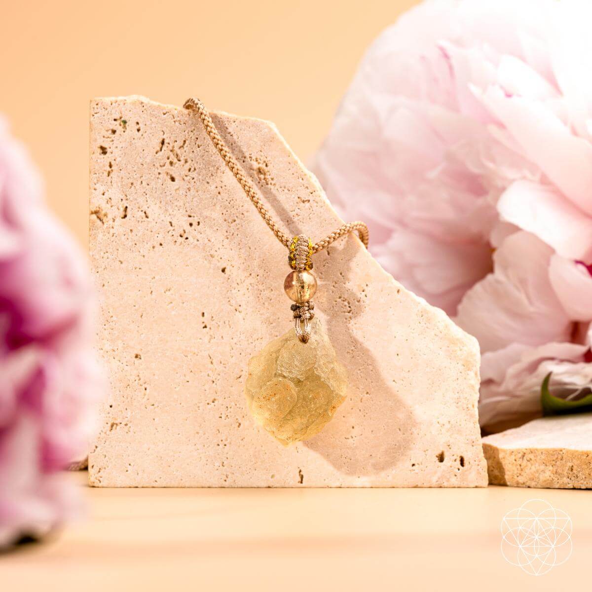 Necklace with a pendant on a stone stand with pink flowers in the background
