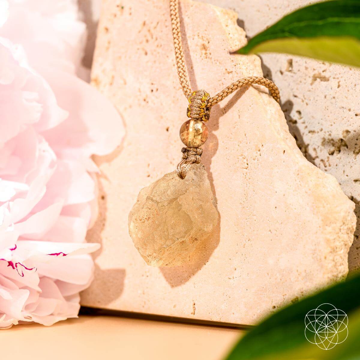 Necklace with a stone pendant on a rock with pink flowers and green leaves.