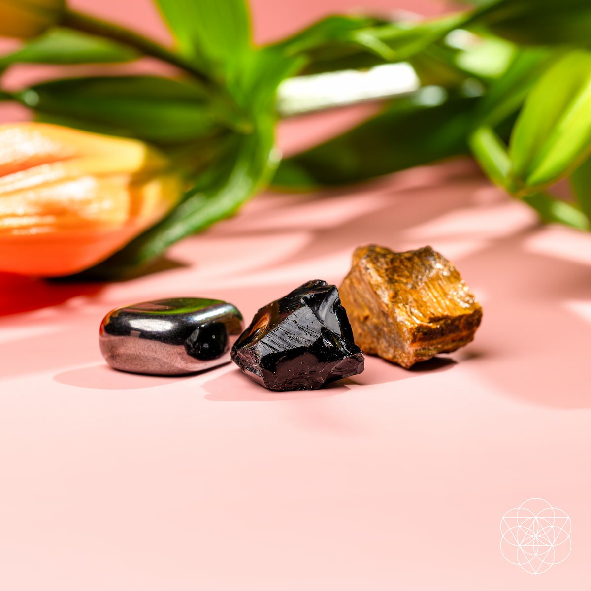 Three rough gemstones on a pink surface with flowers in the background